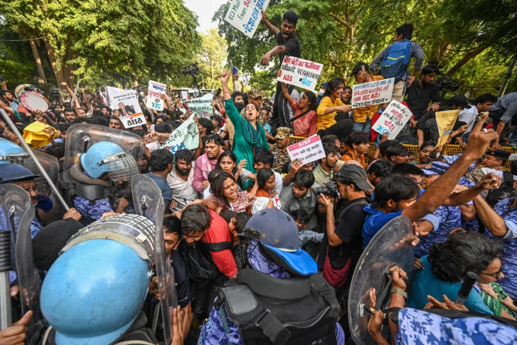 Protesters hold signs during a large demonstration as police in protective gear and riot shields face the crowd in India.