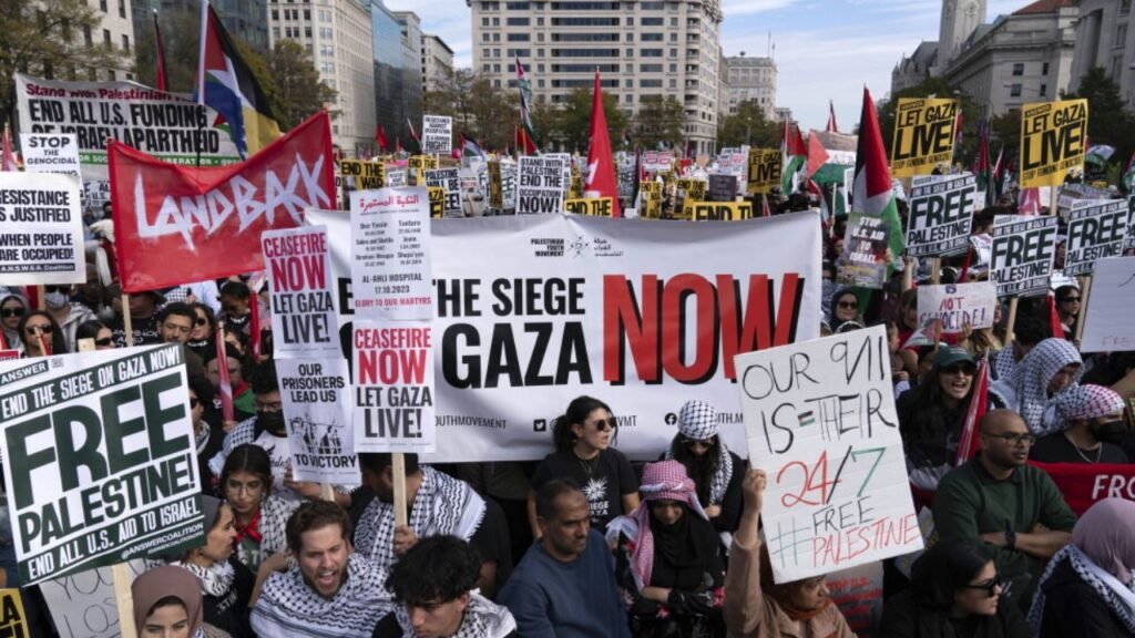 A large pro-Palestinian demonstration fills a city street, with protesters holding Palestinian flags and signs calling for a ceasefire and an end to the siege of Gaza.